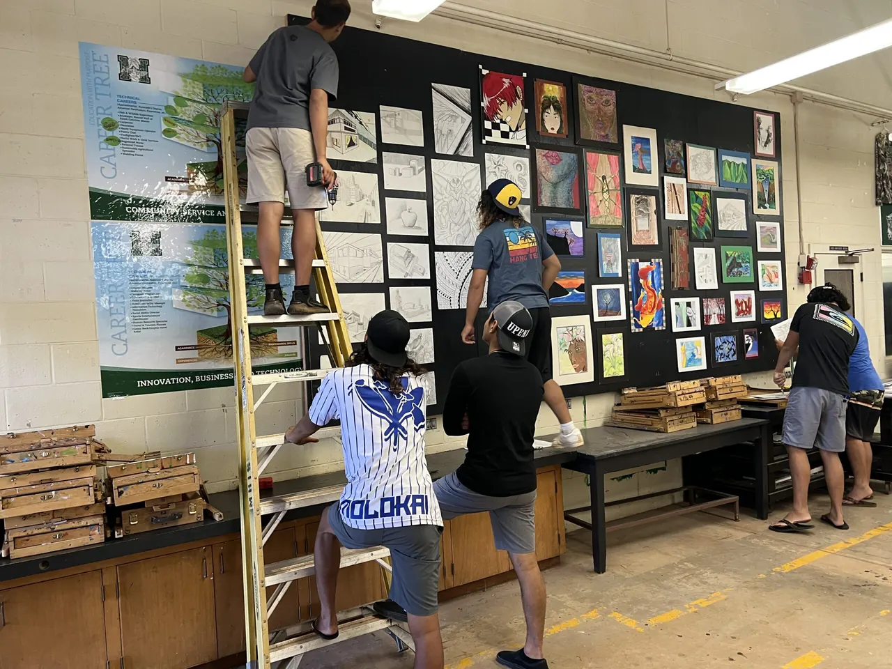 Students putting up a wall of artwork and a career pathways poster in a Molokaʻi High classroom