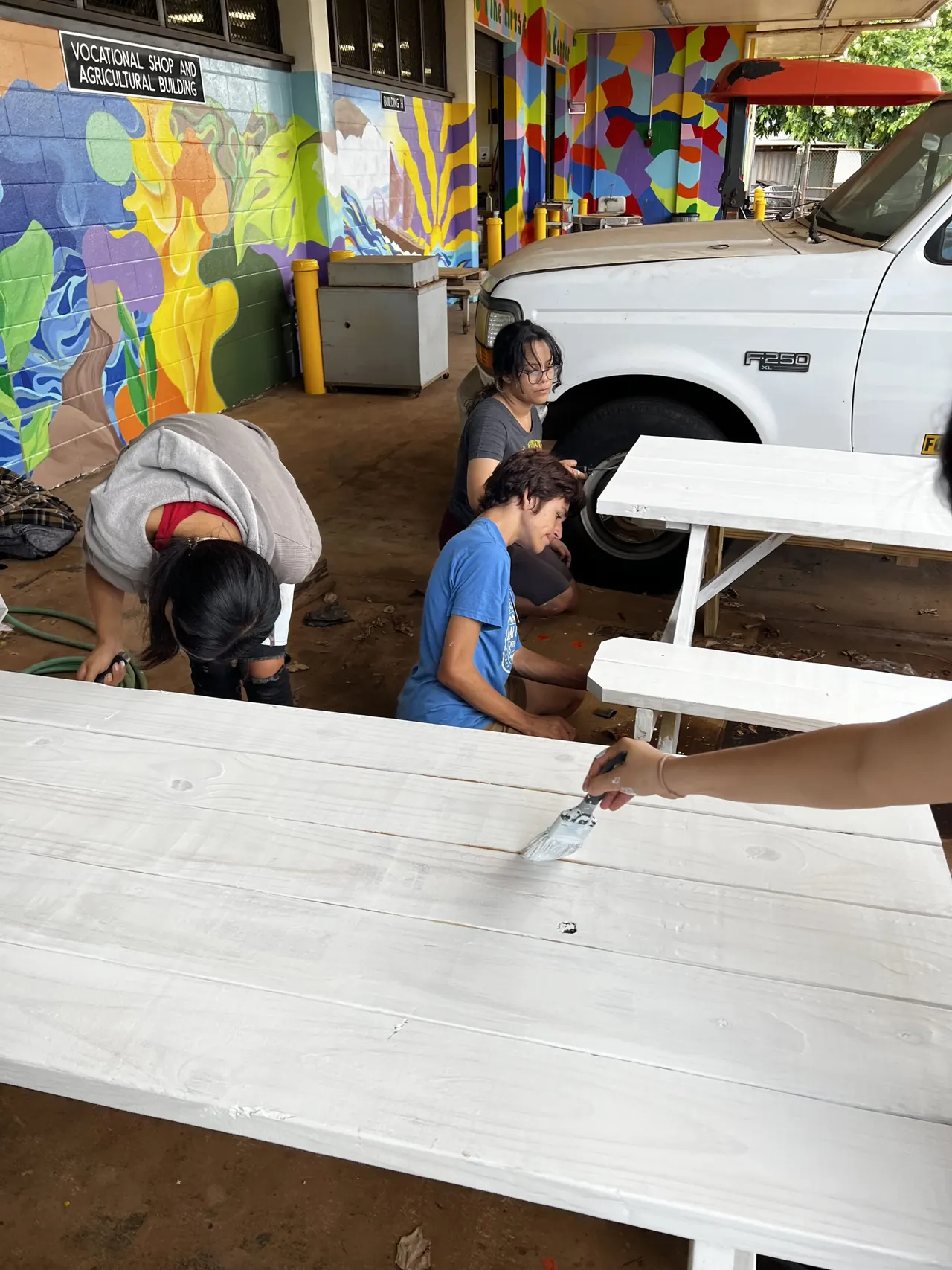 Students painting new white picnic tables outside the vocational shop and agricultural building